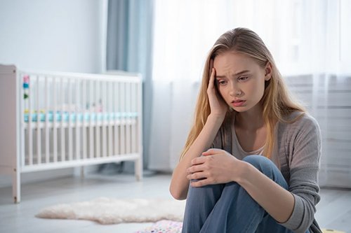 Девушка в депрессии сидит на полу в детской