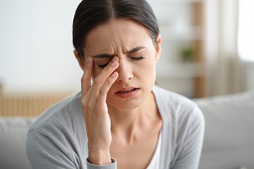 Женщина с головной болью держится за переносицу